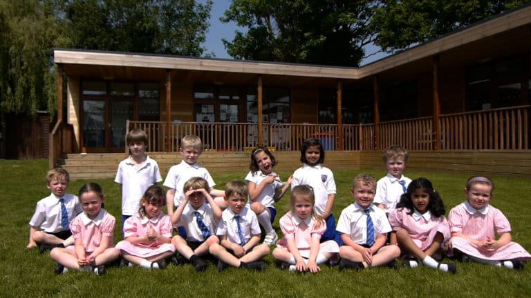 Children sit outside modular eco building at Danesfield School by TGEscapes with cedar cladding and decking